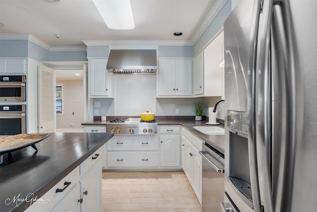 kitchen featuring sink, crown molding, wall chimney exhaust hood, white cabinetry, and stainless steel appliances