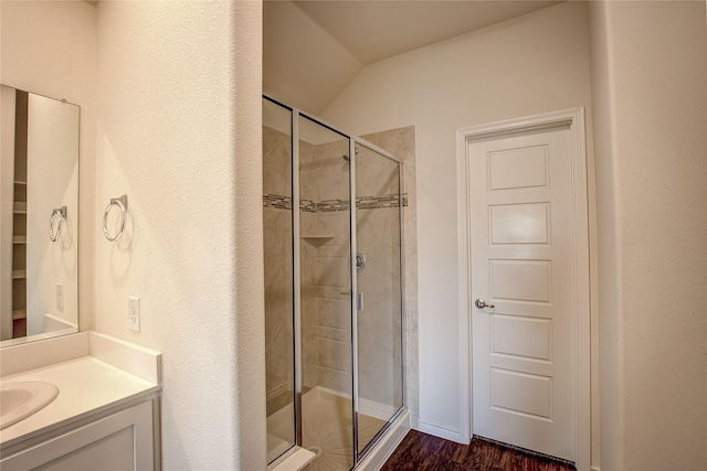 bathroom featuring vanity, a shower with shower door, vaulted ceiling, and wood-type flooring