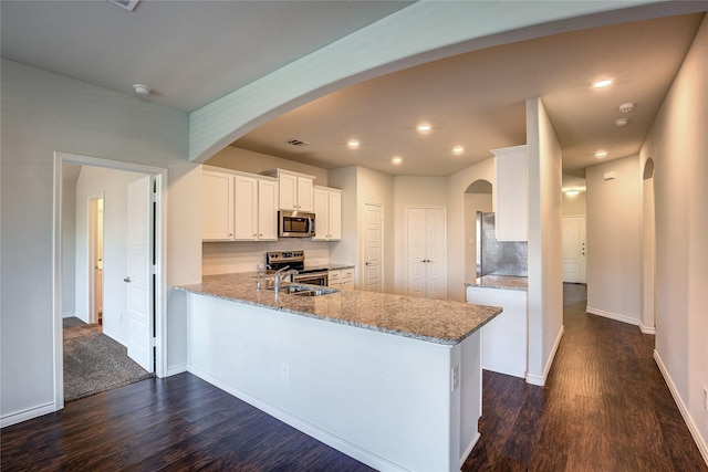 kitchen with white cabinetry, light stone counters, dark hardwood / wood-style flooring, kitchen peninsula, and stainless steel appliances