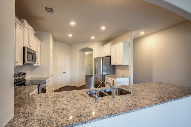 kitchen featuring kitchen peninsula, light stone countertops, stainless steel appliances, sink, and white cabinetry