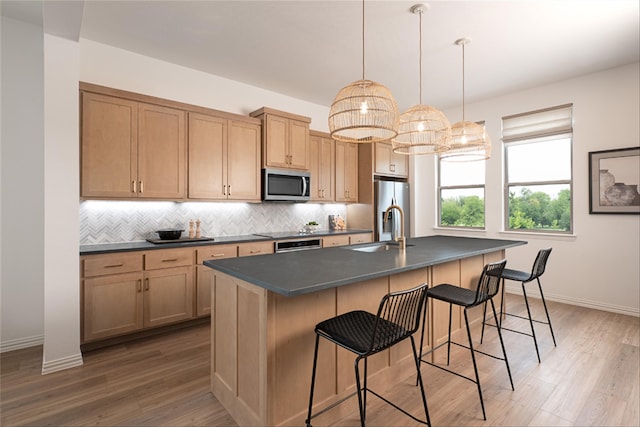 kitchen featuring a kitchen island with sink, sink, decorative backsplash, appliances with stainless steel finishes, and decorative light fixtures