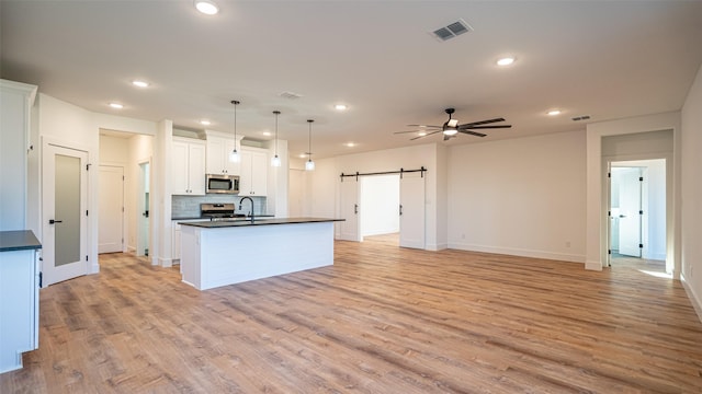 kitchen featuring appliances with stainless steel finishes, decorative light fixtures, light hardwood / wood-style flooring, white cabinetry, and an island with sink