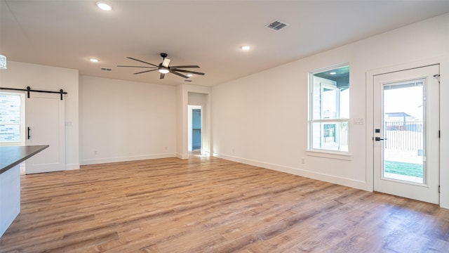 unfurnished living room featuring light wood-type flooring, a barn door, and ceiling fan