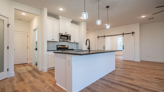 kitchen featuring white cabinetry, sink, stainless steel appliances, tasteful backsplash, and an island with sink