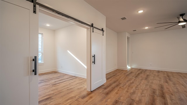 unfurnished room with a barn door, ceiling fan, and light hardwood / wood-style floors