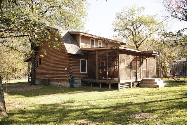 rear view of house featuring a lawn, central AC, a sunroom, and a trampoline