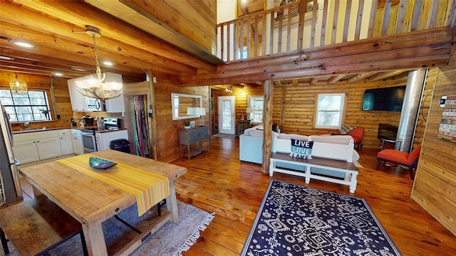 dining area with sink, log walls, wood-type flooring, a chandelier, and a high ceiling