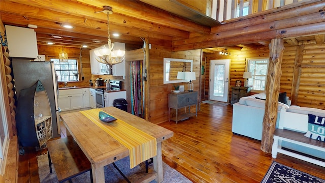 dining room with dark hardwood / wood-style flooring, rustic walls, sink, an inviting chandelier, and beamed ceiling