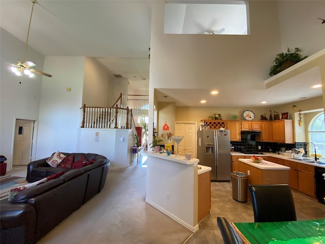 kitchen with ceiling fan, a center island, tasteful backsplash, stainless steel fridge, and a towering ceiling