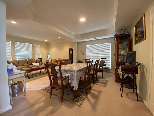 carpeted dining space with a raised ceiling and crown molding