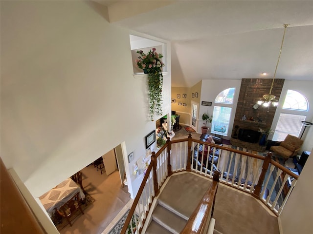 staircase with ceiling fan, high vaulted ceiling, a healthy amount of sunlight, and a brick fireplace