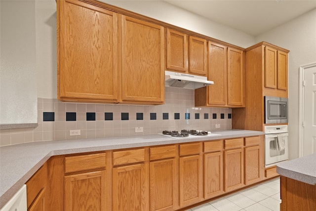 kitchen featuring backsplash, light tile patterned floors, and white appliances