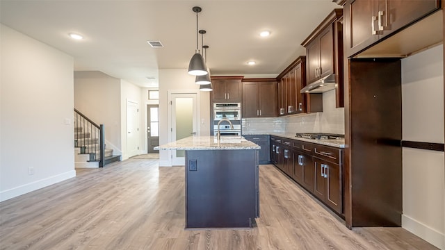 kitchen featuring decorative light fixtures, an island with sink, sink, stainless steel appliances, and light stone countertops