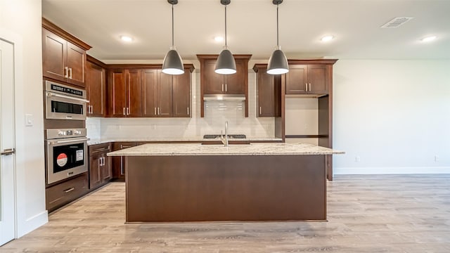 kitchen featuring light stone counters, a kitchen island with sink, tasteful backsplash, and pendant lighting