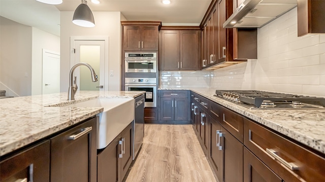 kitchen featuring pendant lighting, sink, appliances with stainless steel finishes, light stone counters, and ventilation hood