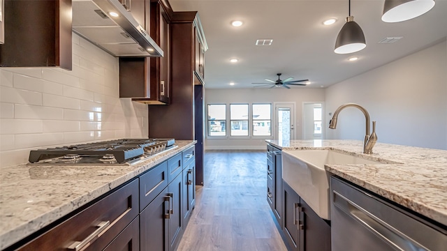 kitchen with light stone counters, dark brown cabinets, exhaust hood, and appliances with stainless steel finishes