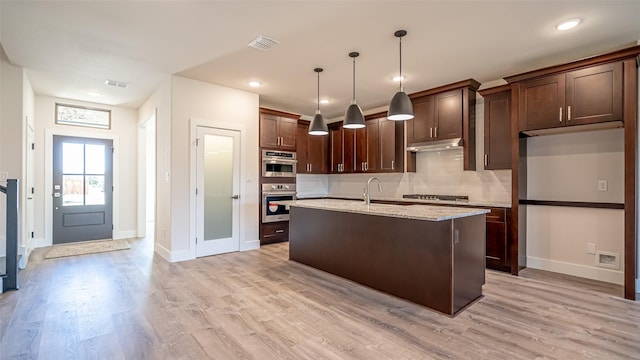 kitchen with sink, light stone counters, hanging light fixtures, an island with sink, and light hardwood / wood-style floors