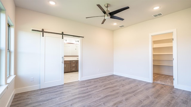 unfurnished bedroom featuring a walk in closet, light hardwood / wood-style flooring, a barn door, and ensuite bathroom