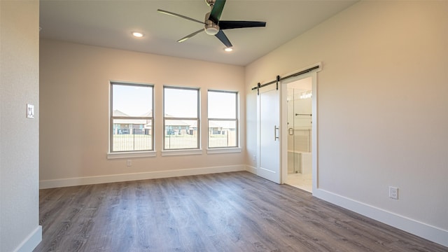 spare room featuring ceiling fan, wood-type flooring, and a barn door