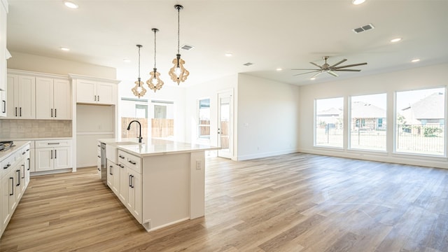 kitchen featuring backsplash, a kitchen island with sink, white cabinets, hanging light fixtures, and ceiling fan