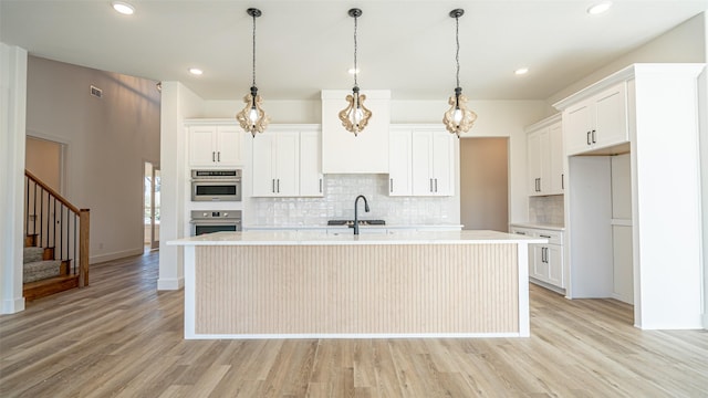 kitchen featuring white cabinets, backsplash, light hardwood / wood-style flooring, and a kitchen island with sink