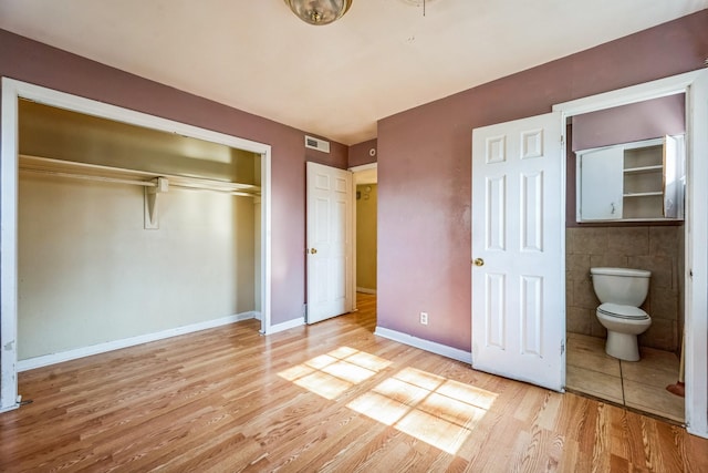 unfurnished bedroom featuring light hardwood / wood-style floors, tile walls, connected bathroom, and a closet