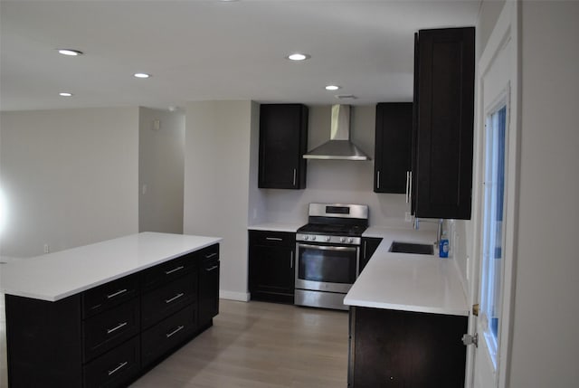 kitchen with a center island, sink, wall chimney exhaust hood, light hardwood / wood-style floors, and stainless steel range oven