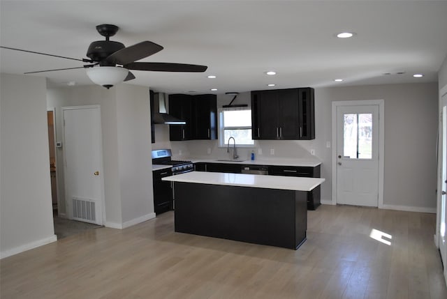 kitchen featuring appliances with stainless steel finishes, wall chimney exhaust hood, sink, light hardwood / wood-style flooring, and a center island