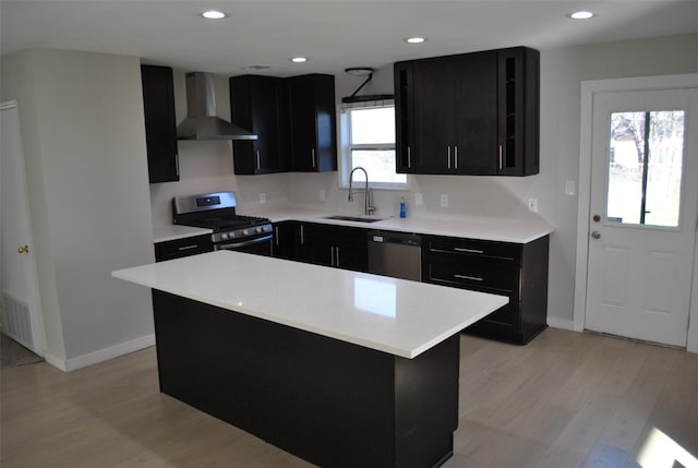 kitchen featuring stainless steel appliances, a healthy amount of sunlight, sink, wall chimney range hood, and a center island