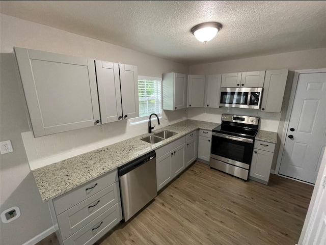 kitchen featuring gray cabinetry, sink, appliances with stainless steel finishes, light hardwood / wood-style floors, and light stone counters