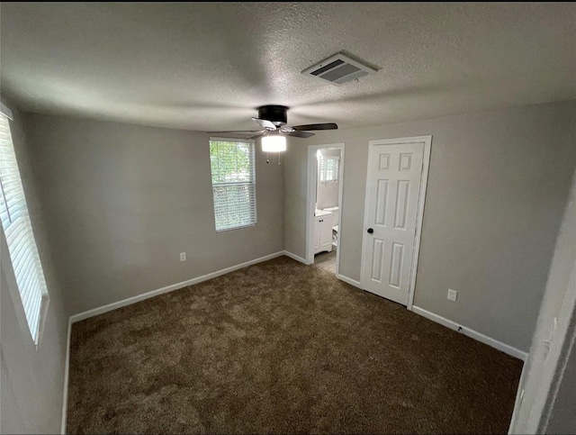 unfurnished bedroom with a textured ceiling, ensuite bath, dark carpet, and ceiling fan