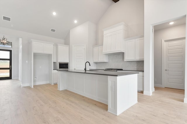 kitchen with white cabinetry, sink, an island with sink, and backsplash