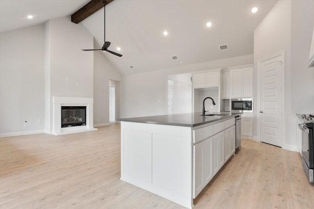 kitchen with appliances with stainless steel finishes, an island with sink, light hardwood / wood-style flooring, and white cabinets