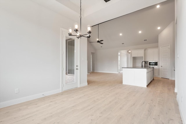 unfurnished living room featuring lofted ceiling, sink, light hardwood / wood-style floors, and an inviting chandelier