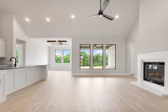 unfurnished living room featuring ceiling fan, high vaulted ceiling, sink, and light wood-type flooring