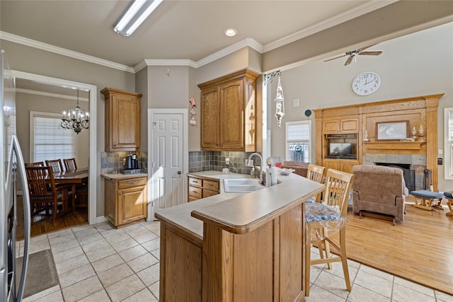 kitchen with ceiling fan with notable chandelier, sink, a fireplace, light tile patterned flooring, and kitchen peninsula