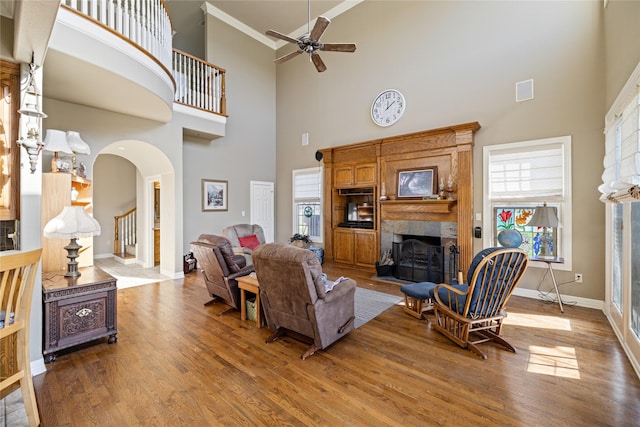 living room with ceiling fan, crown molding, hardwood / wood-style floors, a towering ceiling, and a fireplace