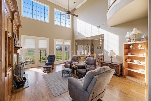 living room with a high ceiling, light wood-type flooring, ceiling fan, and ornamental molding