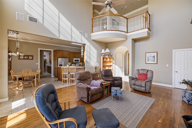 living room featuring hardwood / wood-style floors, ceiling fan with notable chandelier, crown molding, and a high ceiling