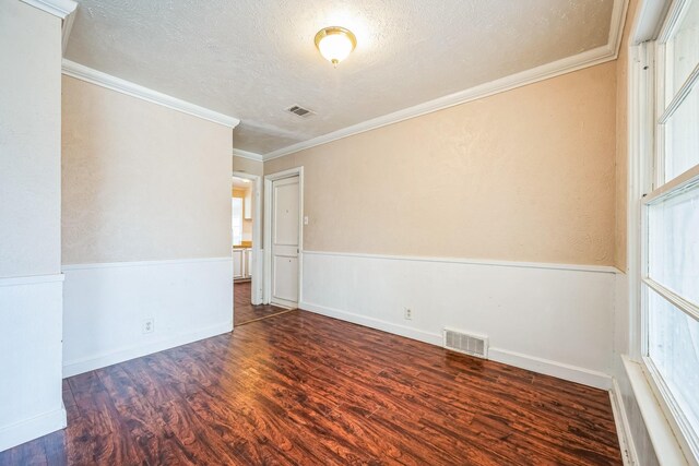 empty room with a textured ceiling, crown molding, and dark wood-type flooring