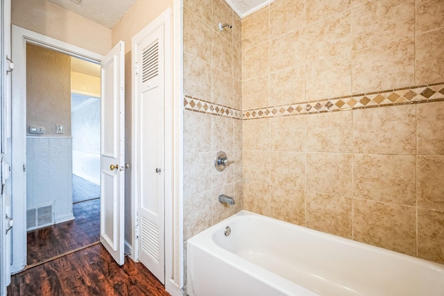 bathroom featuring tiled shower / bath combo, hardwood / wood-style floors, and a textured ceiling