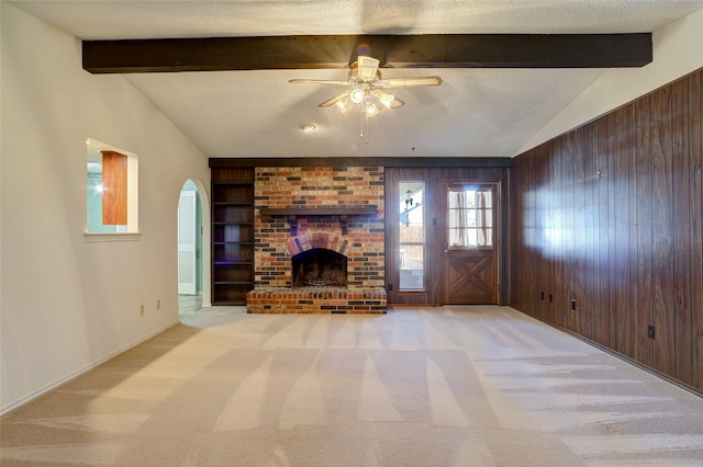 unfurnished living room featuring ceiling fan, a brick fireplace, light colored carpet, a textured ceiling, and wooden walls