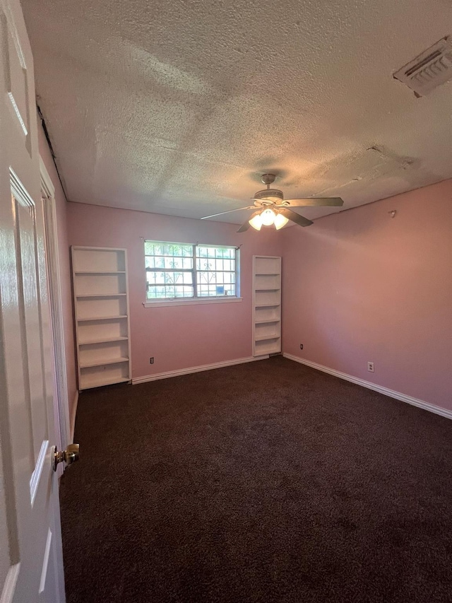 carpeted empty room with built in shelves, ceiling fan, and a textured ceiling