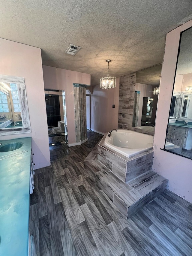 bathroom with hardwood / wood-style flooring, vanity, a relaxing tiled tub, and a textured ceiling