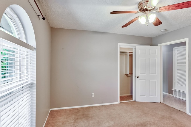 unfurnished bedroom featuring ceiling fan, light colored carpet, a closet, and a textured ceiling