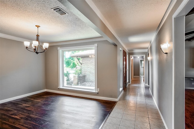 hall with tile patterned flooring, ornamental molding, a textured ceiling, and a notable chandelier