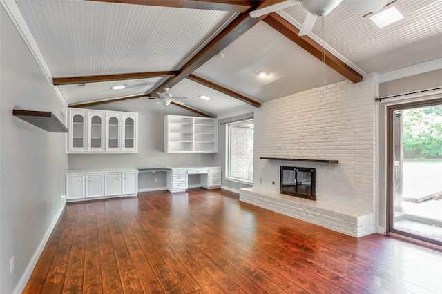 unfurnished living room with dark hardwood / wood-style floors, built in desk, a fireplace, vaulted ceiling with beams, and ceiling fan