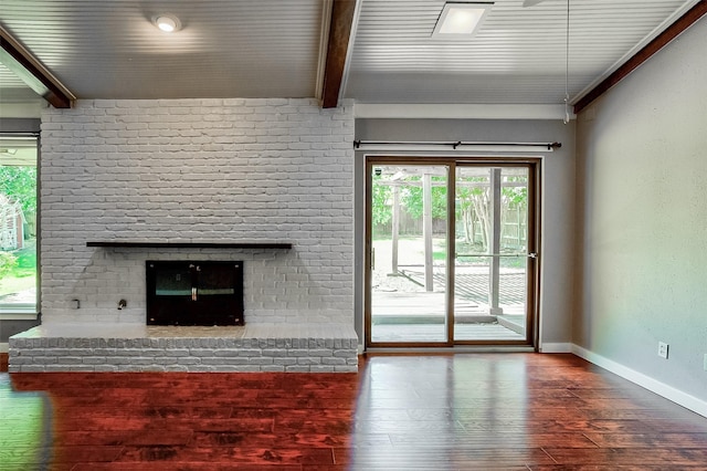 unfurnished living room with beamed ceiling, hardwood / wood-style floors, a brick fireplace, and plenty of natural light