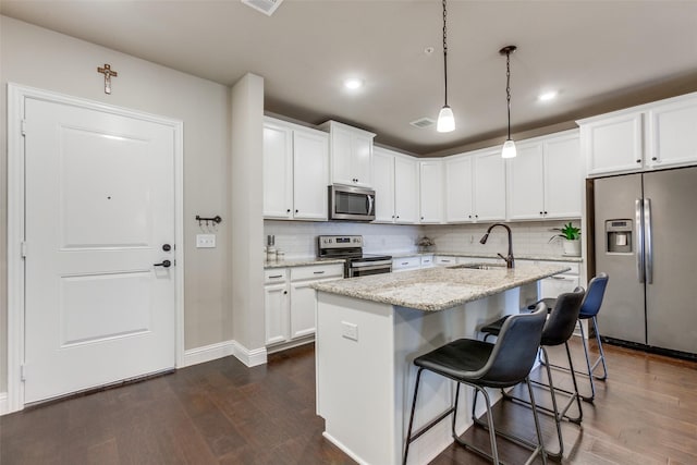 kitchen featuring a kitchen island with sink, hanging light fixtures, sink, light stone countertops, and stainless steel appliances