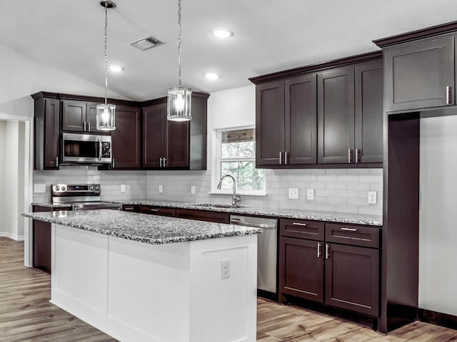 kitchen with appliances with stainless steel finishes, lofted ceiling, hanging light fixtures, and a kitchen island